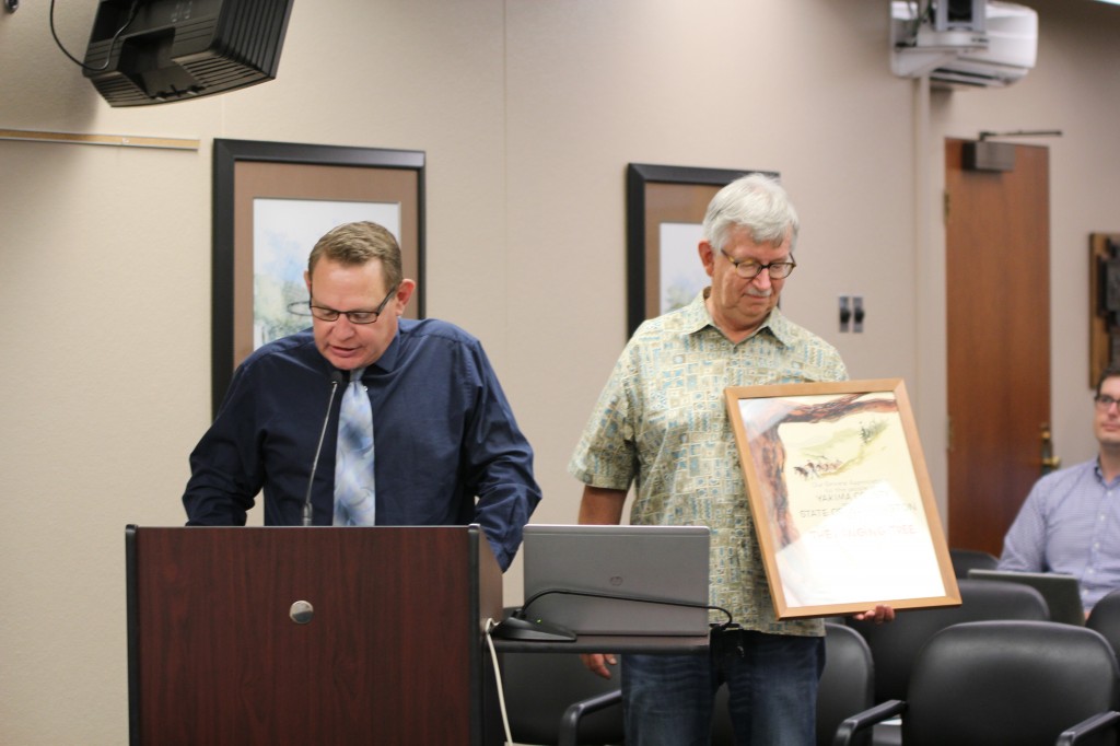 Communications & Public Affairs Director Randy Beehler addresses the Yakima City Council as Yakima Valley Museum Director John Ball looks at an original signed poster from the classic movie “The Hanging Tree” that was recently donated to the Museum by The City of Yakima.