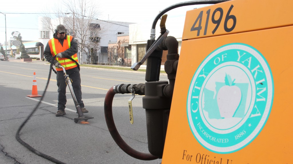 City Street Maintenance Specialist Brady Willis uses a heat lance to clear debris from cracks and voids on Yakima Avenue before filling them with tar to help prevent future pavement problems. 