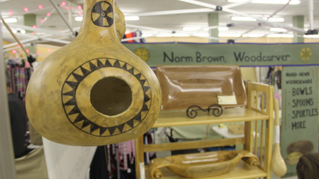 A hollowed and decorated birdhouse gourd hangs in front of many interesting wood carvings at Norm Brown, Woodcarvers booth at the Indoor Farmers Market on 3rd Street in Downtown Yakima. The Indoor Farmers Market is open on Thursdays 3pm to 6pm as well as Saturdays and Sundays from 10am to 4:00pm.