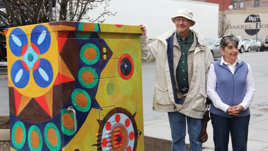 Local artist Stan Hughes and Yakima Arts Commission Chair Noel Moxley stand next to the first installation of the Yakima Arts Commission's latest project, which wraps plain traffic signal boxes in colorful public art.